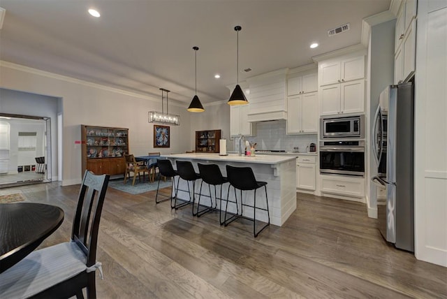 kitchen with decorative backsplash, light countertops, a kitchen bar, appliances with stainless steel finishes, and visible vents
