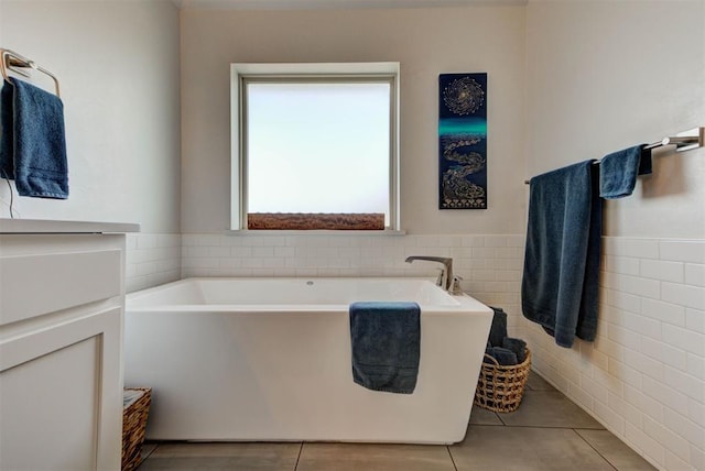 full bathroom with tile walls, a soaking tub, tile patterned flooring, and wainscoting