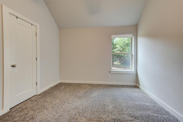 carpeted spare room featuring vaulted ceiling and baseboards