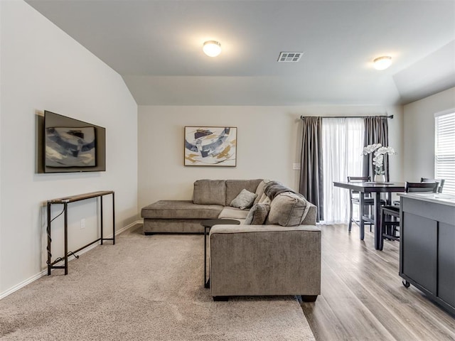 living area featuring lofted ceiling, baseboards, and light wood finished floors