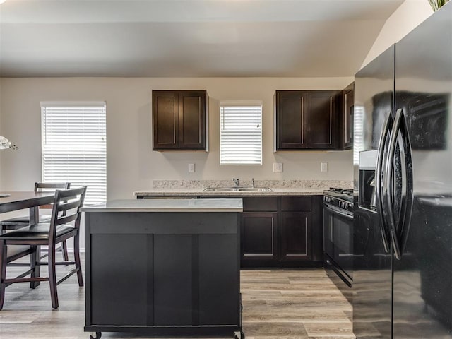 kitchen featuring black appliances, a kitchen island, light wood-type flooring, a sink, and light countertops