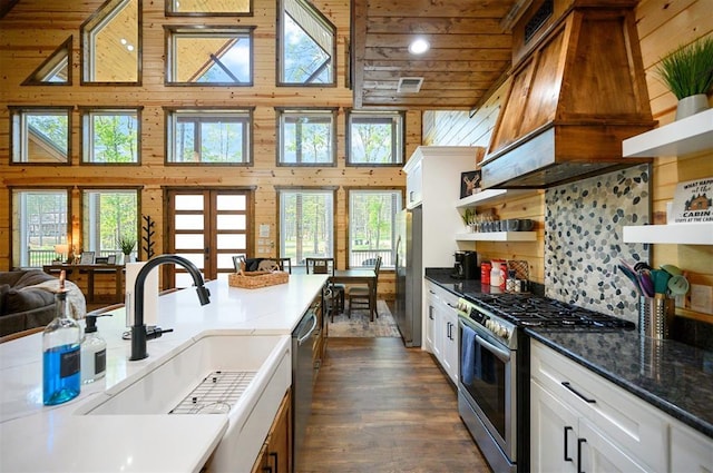 kitchen featuring a sink, a high ceiling, open shelves, wooden walls, and appliances with stainless steel finishes