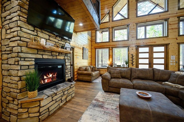 living room featuring high vaulted ceiling, a healthy amount of sunlight, wooden walls, and a fireplace