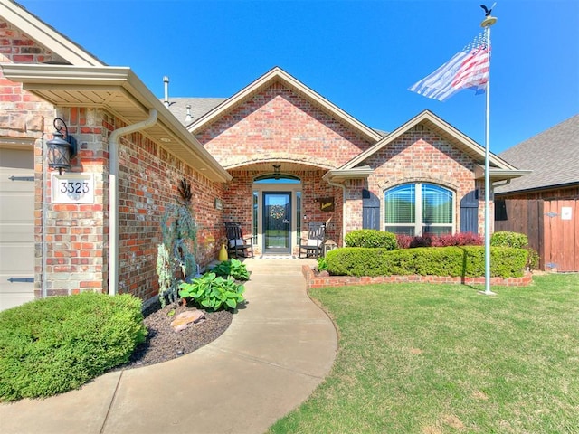 property entrance with brick siding, fence, and a yard