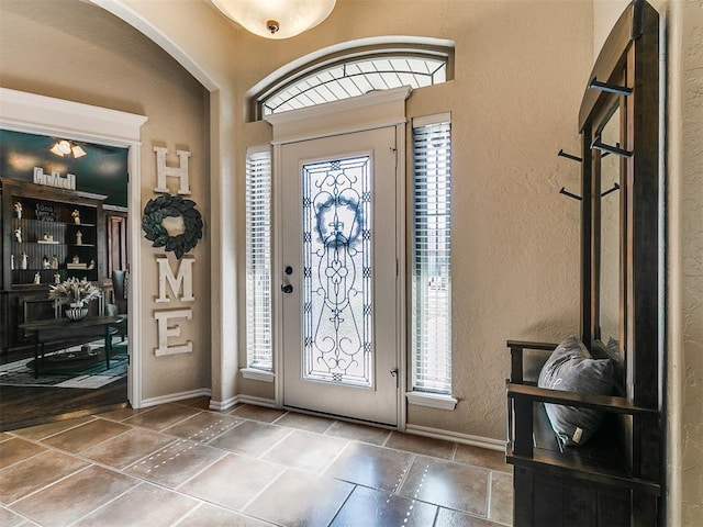 foyer featuring arched walkways, a textured wall, and baseboards