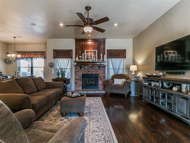 living area with a textured ceiling, a brick fireplace, wood finished floors, ceiling fan with notable chandelier, and recessed lighting