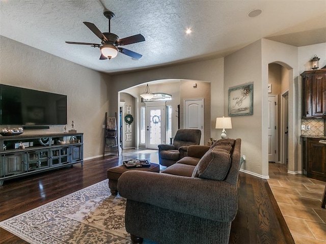 living room with arched walkways, a ceiling fan, baseboards, and a textured ceiling