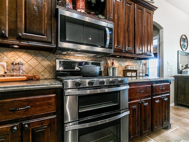 kitchen with dark brown cabinetry, light tile patterned flooring, tasteful backsplash, arched walkways, and appliances with stainless steel finishes
