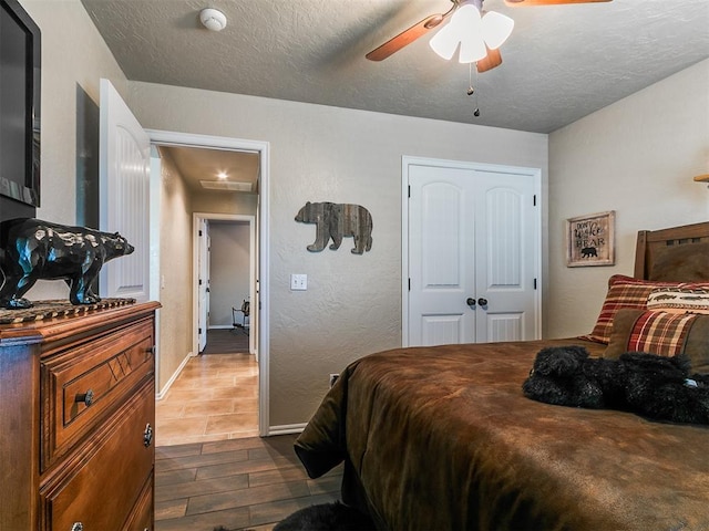 bedroom with ceiling fan, a textured ceiling, dark wood finished floors, baseboards, and a closet