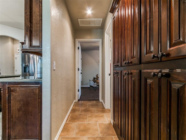 hallway with baseboards, a textured wall, light tile patterned flooring, and visible vents