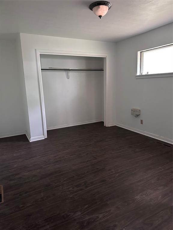 unfurnished bedroom featuring baseboards, dark wood-type flooring, and a closet