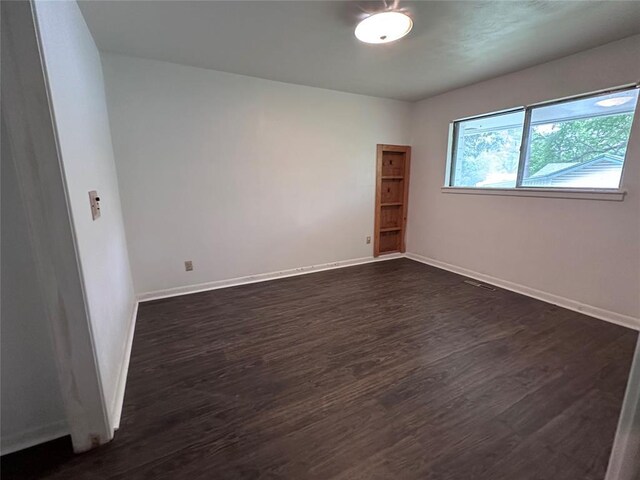 unfurnished room with baseboards, dark wood-type flooring, and visible vents
