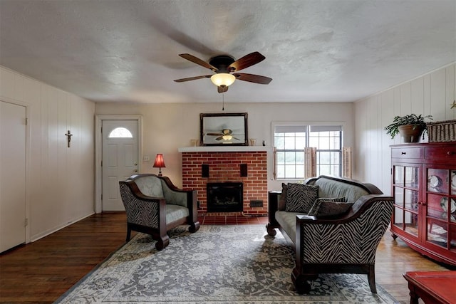 living area with a brick fireplace, wood finished floors, and ceiling fan