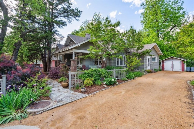 view of front facade featuring dirt driveway, covered porch, a storage unit, an outdoor structure, and a detached garage
