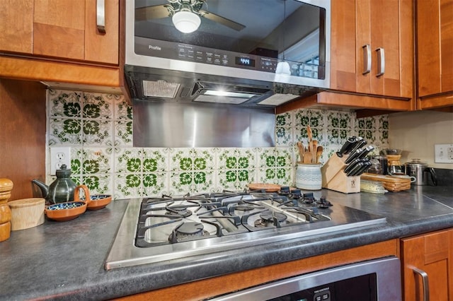 kitchen with stainless steel gas stovetop, oven, brown cabinetry, dark countertops, and range hood