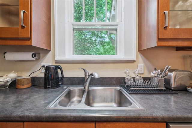 kitchen view of a sink, dark countertops, glass insert cabinets, and brown cabinetry