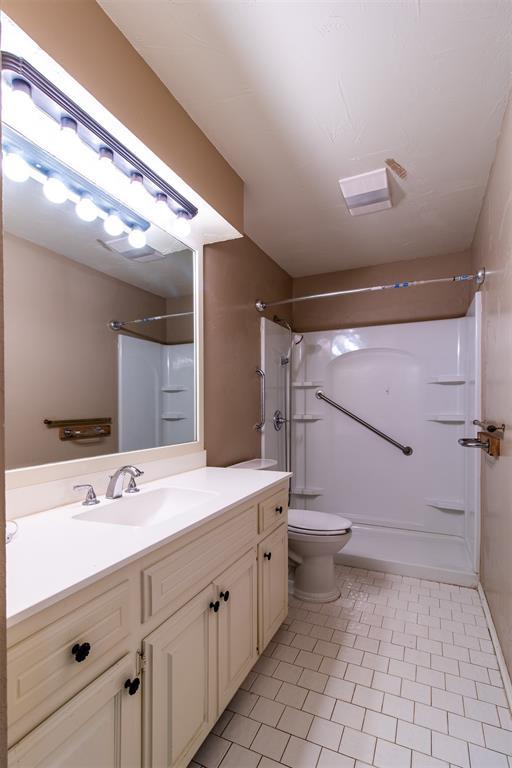 bathroom featuring toilet, tile patterned floors, walk in shower, and vanity