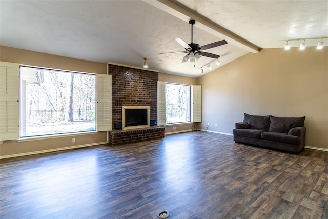 living room with a ceiling fan, a fireplace, rail lighting, lofted ceiling with beams, and dark wood finished floors