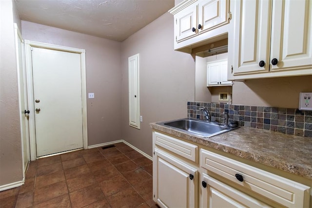 kitchen with backsplash, baseboards, visible vents, and a sink