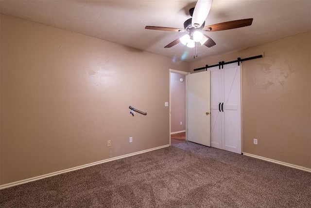 unfurnished bedroom with carpet floors, baseboards, a barn door, and ceiling fan