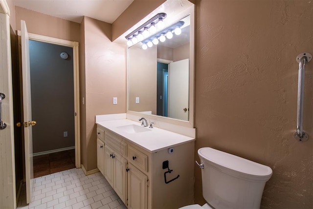 bathroom with toilet, tile patterned floors, a textured wall, and vanity