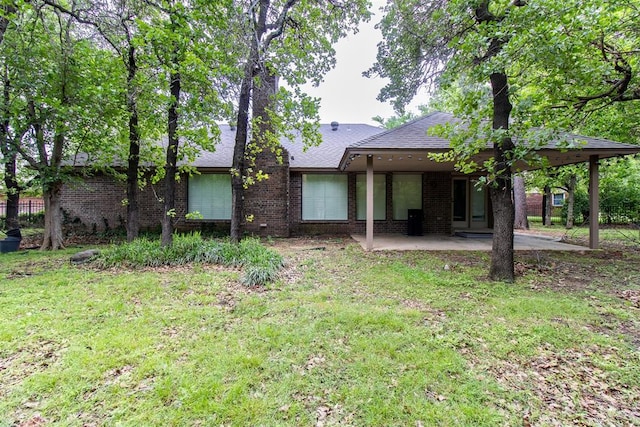 back of house featuring brick siding, a shingled roof, a patio area, and a lawn