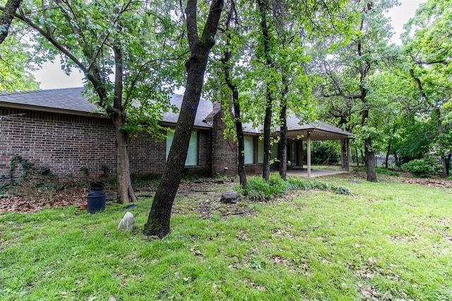 back of property with a yard, brick siding, a patio, and roof with shingles
