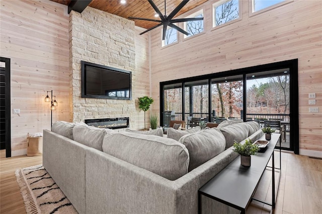 living area with wood ceiling, ceiling fan, a stone fireplace, wooden walls, and a high ceiling
