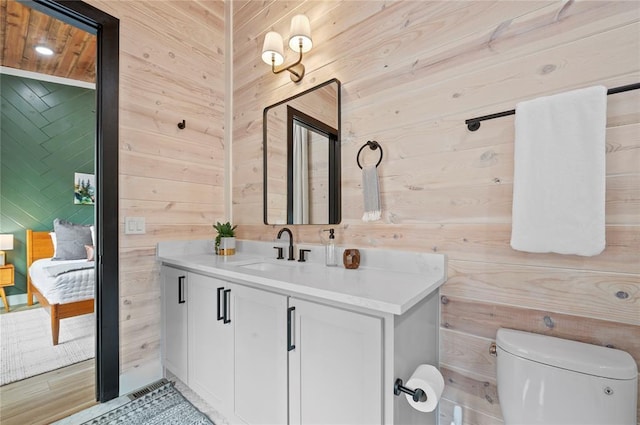 ensuite bathroom featuring wooden walls, toilet, ensuite bath, and vanity