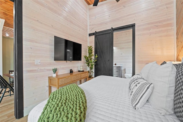 bedroom with a barn door, wood ceiling, wood finished floors, and wooden walls