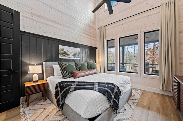bedroom with wooden walls, a ceiling fan, light wood-type flooring, and a towering ceiling
