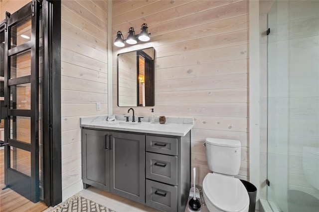 full bath with vanity, wood walls, a shower with shower door, and toilet