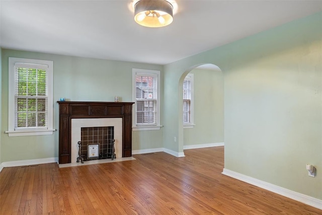 unfurnished living room featuring plenty of natural light, arched walkways, baseboards, and wood finished floors