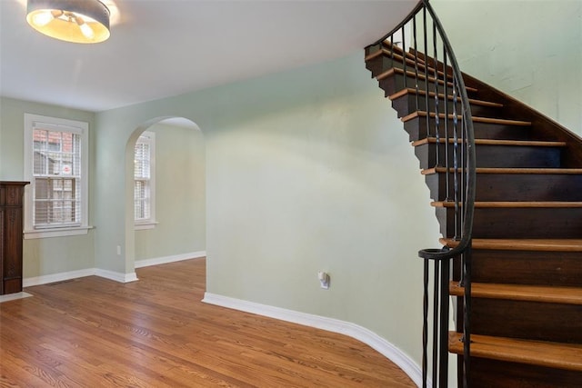 stairway with baseboards, arched walkways, and wood finished floors