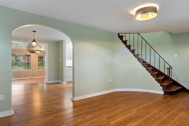 interior space featuring stairs, arched walkways, baseboards, and wood finished floors