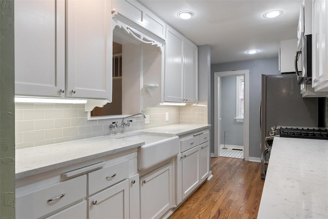 kitchen featuring tasteful backsplash, light wood-type flooring, a sink, baseboards, and white cabinets