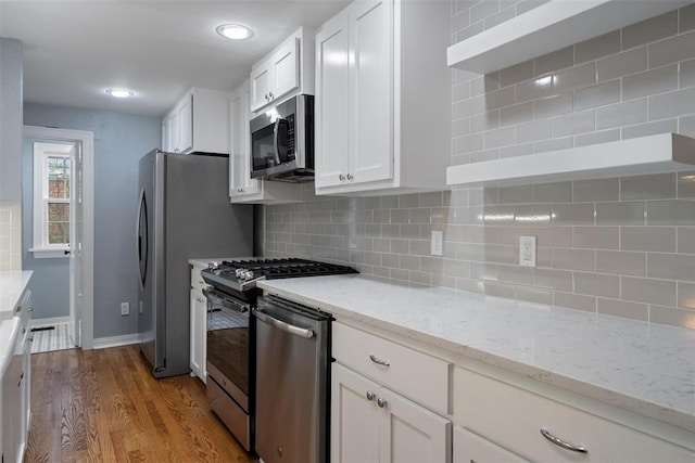 kitchen featuring white cabinets, open shelves, appliances with stainless steel finishes, light stone counters, and light wood-style floors