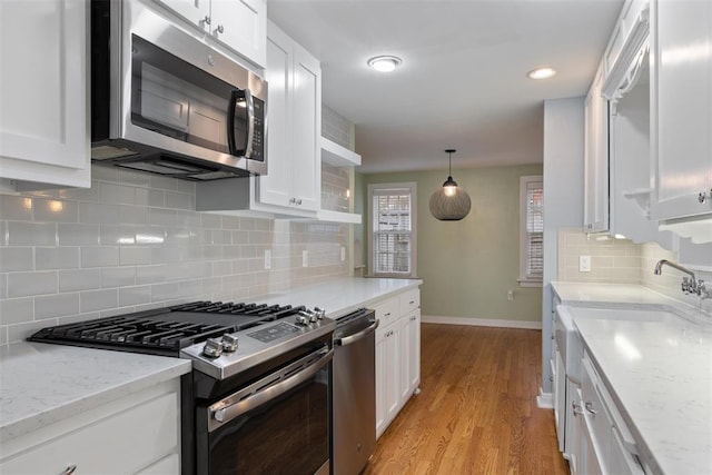 kitchen with white cabinets, stainless steel appliances, backsplash, and light wood-type flooring