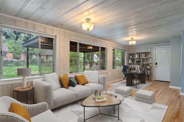 living area with crown molding, wood walls, baseboards, wooden ceiling, and light wood finished floors