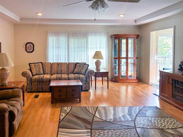 living room featuring light wood finished floors, a raised ceiling, ceiling fan, and crown molding
