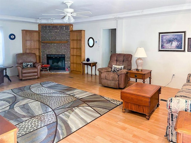 living area featuring a ceiling fan, ornamental molding, wood finished floors, and a fireplace