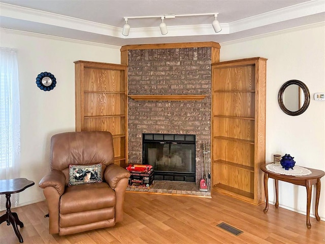 living area with a fireplace, wood finished floors, visible vents, and ornamental molding