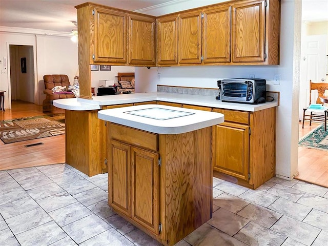 kitchen featuring brown cabinetry, a toaster, a kitchen island, and light countertops