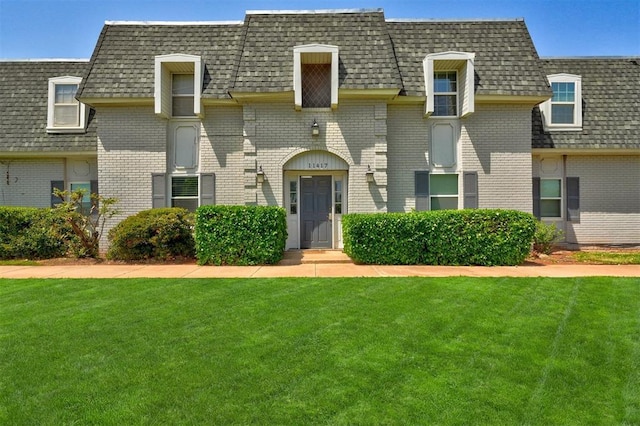view of front of home featuring brick siding, roof with shingles, mansard roof, and a front yard