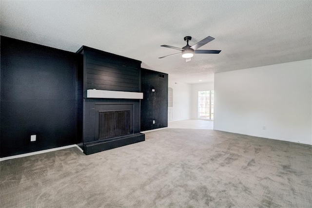unfurnished living room featuring ceiling fan, a textured ceiling, a large fireplace, baseboards, and carpet