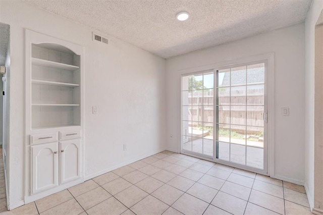 empty room featuring visible vents, built in features, baseboards, a textured ceiling, and light tile patterned floors