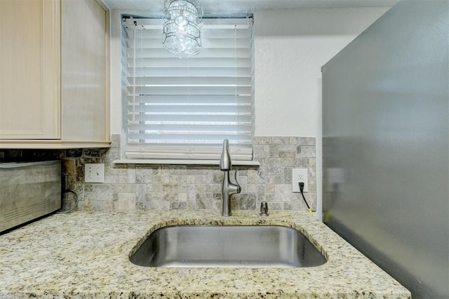 kitchen featuring a sink, light stone counters, and backsplash