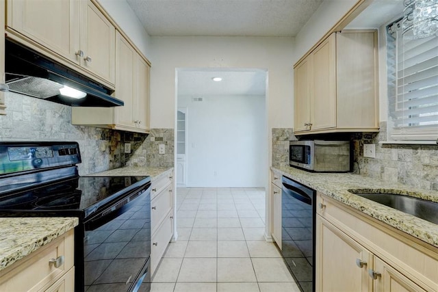 kitchen with under cabinet range hood, tasteful backsplash, light stone counters, light tile patterned floors, and black appliances