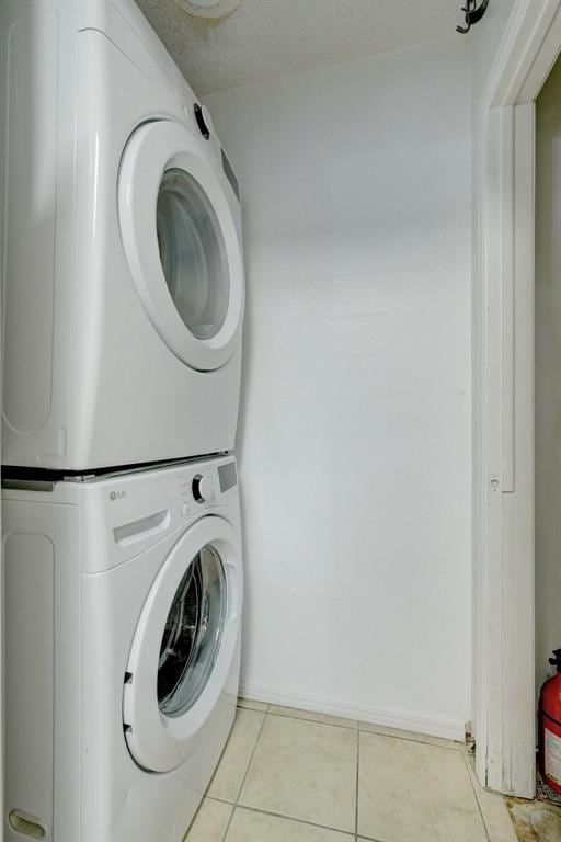 washroom featuring light tile patterned flooring, stacked washer / drying machine, baseboards, and laundry area