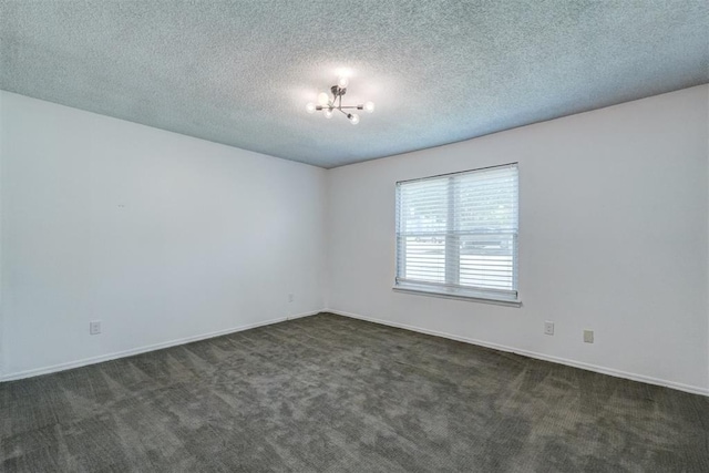 spare room featuring baseboards, dark carpet, a textured ceiling, and a notable chandelier